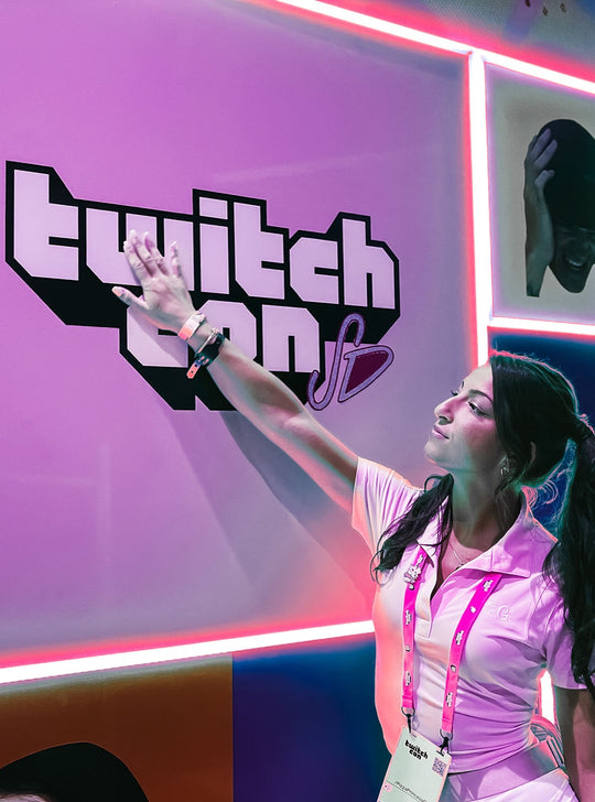 G in pink reaching toward a glowing TwitchCon sign