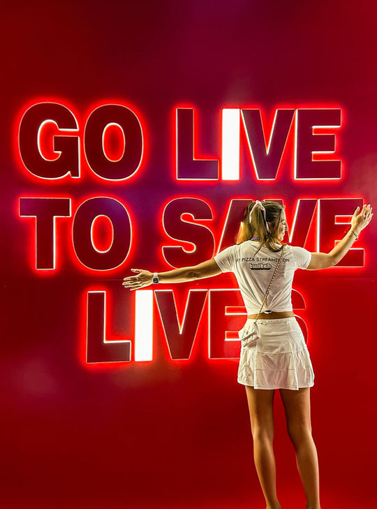 G with arms open in front of a red neon sign: Go live to save lives