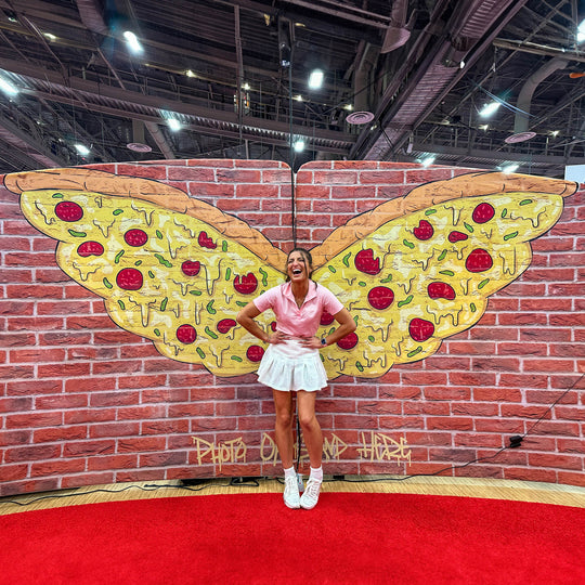 G posing in front of a painted mural of pizza-slice wings on a brick wall