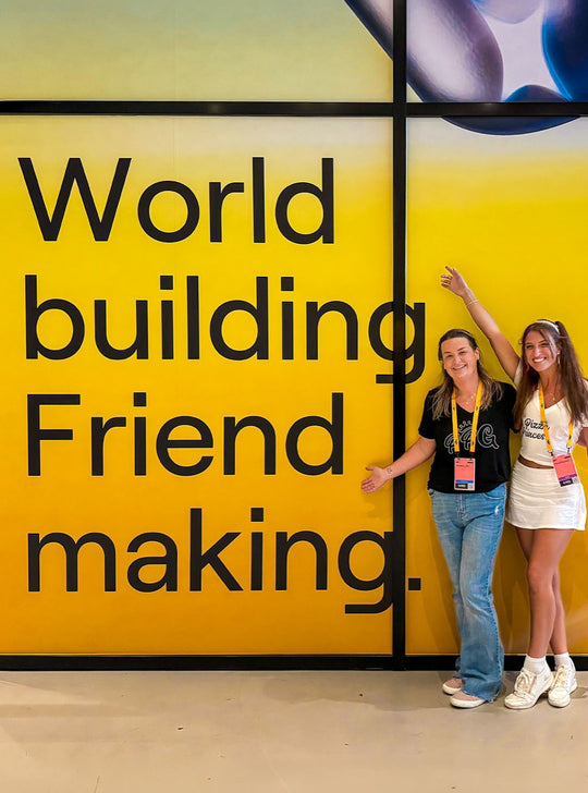 G and a friend at a yellow wall that reads "World building. Friend making."